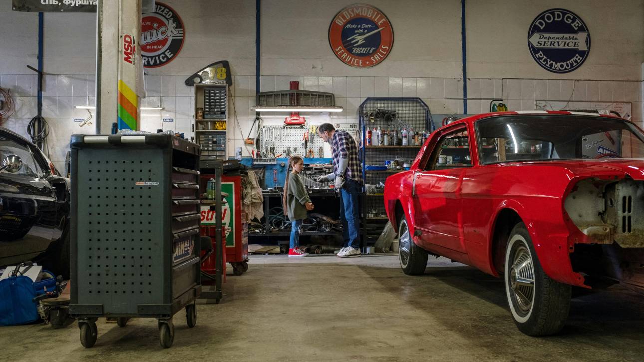 Grandfather and Granddaughter working in a car garage with red car
